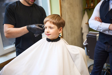 Skilled barber using professional hair trimmer to remove hair from boys headの写真素材