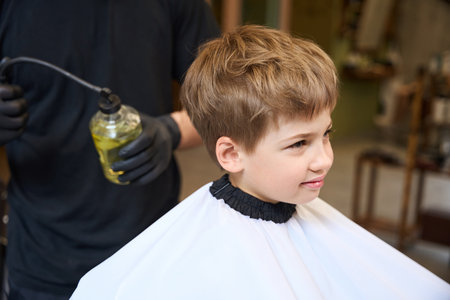 Skilled barber applying aroma spray from on little boy hairの写真素材