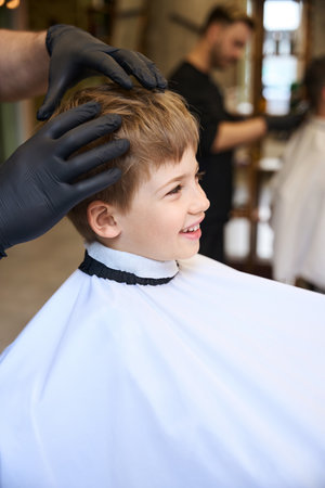 Attractive little boy sincerely laughing sitting in barber shopの写真素材