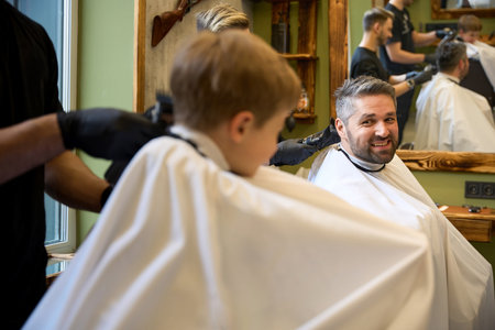 Qualified barber using hair trimmer to cut boys hairの写真素材