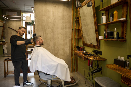 Skilled barber combing bearded adult man hair and cutting splitted endsの写真素材
