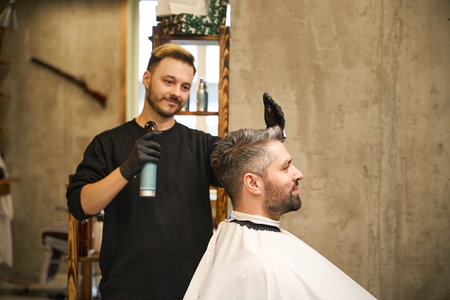 Smiling hairstylist applying cologne or fixing spray on clients haircutの写真素材