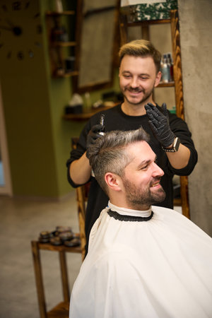 Positive bearded barber spraying fixing liquid into the man haircutの写真素材