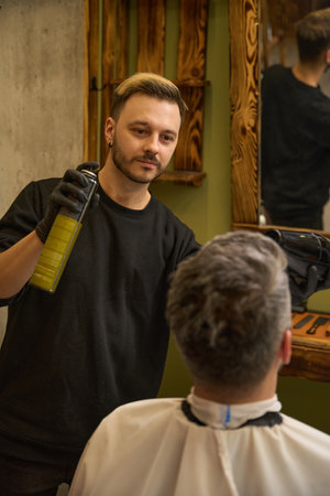 Barber applying fixing spray into hair and drying with hair dryerの写真素材