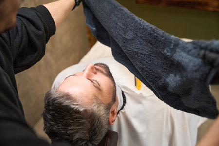 Barber preparing hot towel to apply it on clients chin and neckの写真素材