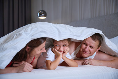 Dad and mom with little daughter in hut made of blanketsの写真素材