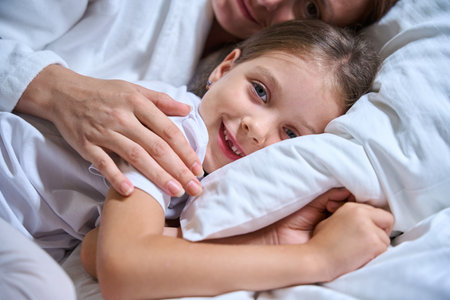 Little girl and her mother are lying on large cozy bedの写真素材
