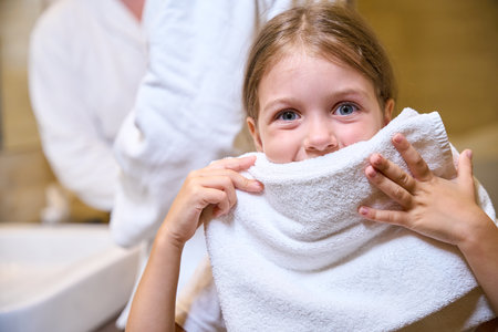 Pretty little girl wipes her face with a fluffy towelの写真素材