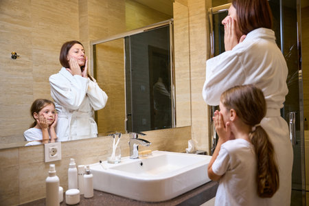 Woman and little girl wash themselves in front of mirrorの写真素材