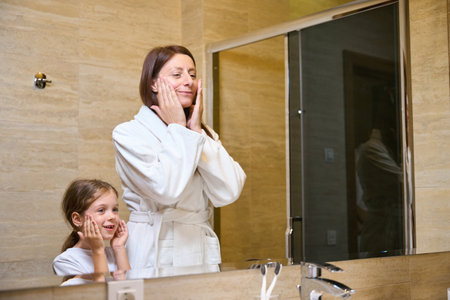 Young woman and little girl wash themselves in front of mirrorの写真素材