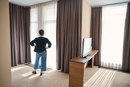 Back view of adult Caucasian woman posing in hotel room near big windowの写真素材