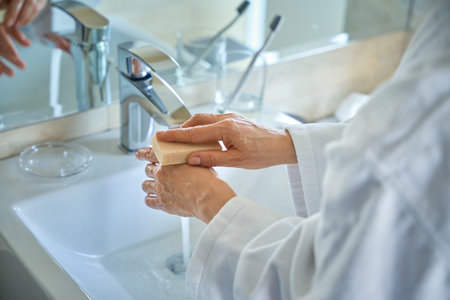 Cropped photo of woman in bathrobe washing hands with soap in bathroomの写真素材