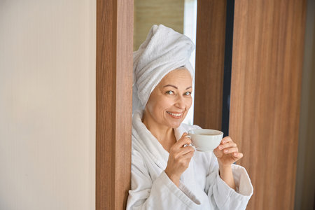 Dreamy adult woman in white bathrobe enjoying tea holding cupの写真素材