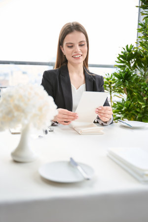 Smiling young woman holding menu, reading, sitting in the restaurantの写真素材