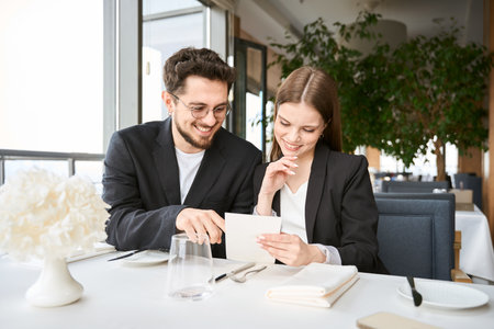 Happy lovely couple choosing dishes from the menu sitting in the restaurantの写真素材