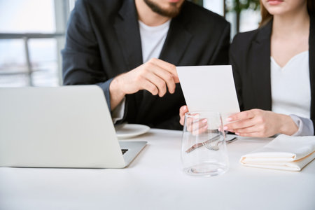 Young man and woman using laptop during business meeting, holding menuの写真素材