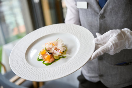 Male waiter in uniform carrying plate of salad in a restaurant