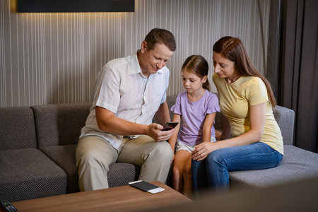 Parents and daughter are sitting on sofa in hotel roomの写真素材