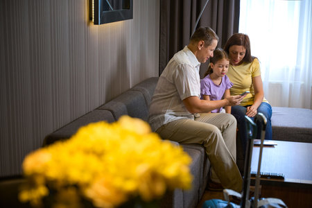 Hotel guests with their little daughter sit on cozy sofaの写真素材