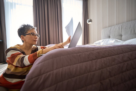 Adult businesswoman working with laptop holding documents sitting on the floor in hotelの写真素材