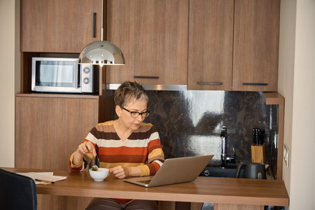 Mature woman enjoying tea and working with laptop sitting at the table in hotelの写真素材