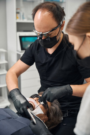 Surgeon and his assistant remove a tooth from elderly ladyの写真素材