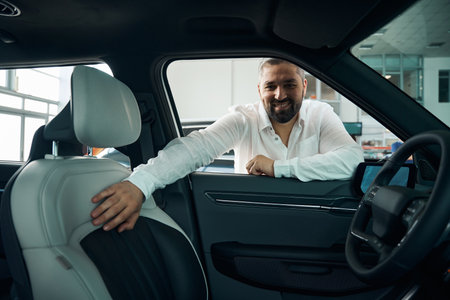 Portrait of Caucasian man in white shirt examining auto at showroom store
