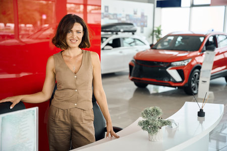 Saleswoman posing at the dealership showroom, new cars on the backgroundの写真素材