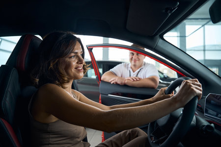 Salesman manager showing female customer new car in showroomの写真素材