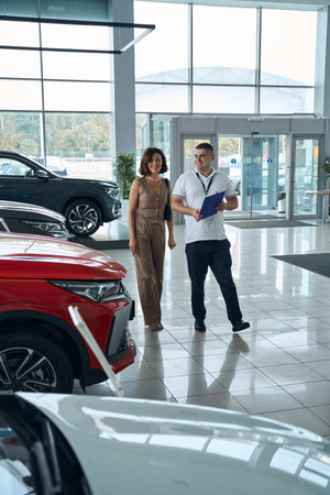 Salesman manager with file folder and female customer standing in car showroomの写真素材