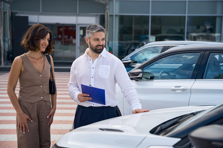 Salesman manager showing new car for woman at car salon showroom outdoorsの写真素材
