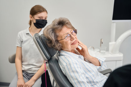 Elderly lady at dentists office complains to specialist about toothacheの写真素材