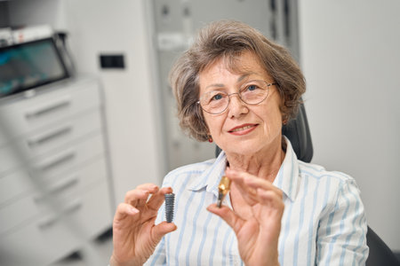 Elderly woman at appointment examines model of components of adental implantの写真素材