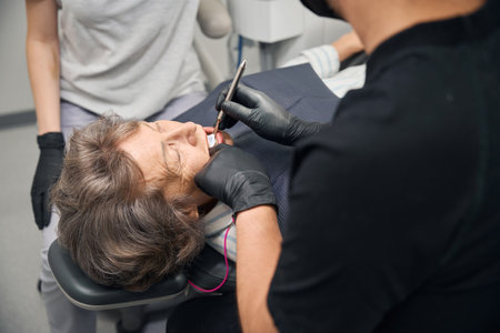 Doctor examines an elderly ladys teeth using a dental mirrorの写真素材