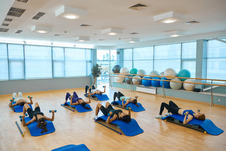 Health group performs strength exercises with dumbbells, lying on special platformsの写真素材