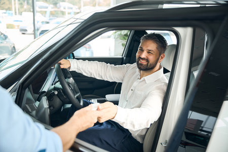 Happy adult businessman receiving car key from salesman at the dealership showroomの写真素材