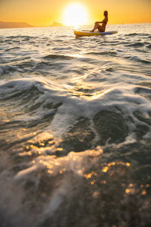 Relaxed young woman paddleboarding at ocean sunriseの写真素材