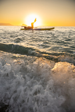 Serene young woman doing yoga on paddleboard at sunrise