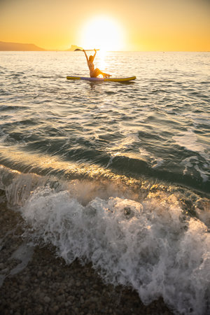 Young woman paddleboarding peacefully at sunrise on ocean