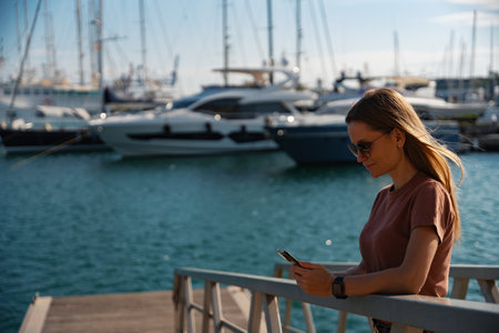 Young pretty woman in sunglasses typing on smartphone posing at the pier in the port, Valenciaの写真素材