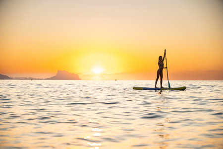 Young woman stand-up paddleboarding at ocean during sunset