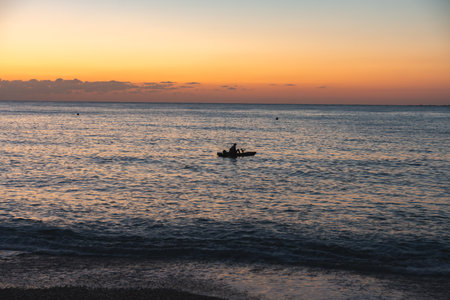Contemplative man fishing in small boat at sunset on oceanの写真素材