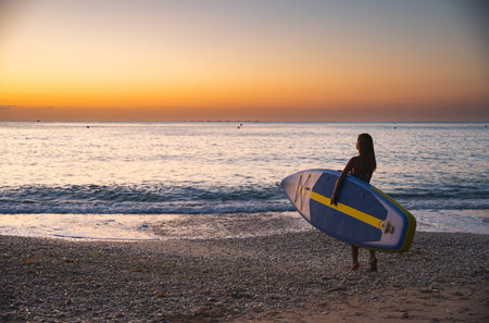 Young woman carrying paddleboard at beach during sunsetの写真素材
