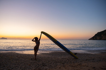 Serene woman paddleboarding at beach during sunsetの写真素材