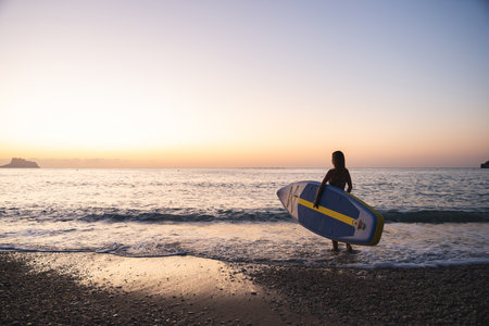 Young woman paddleboarding at serene beach during sunrise