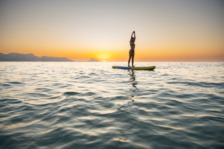 Young woman paddleboarding on calm ocean at sunsetの写真素材