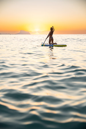 Young woman paddleboarding in ocean at sunset, serene mood