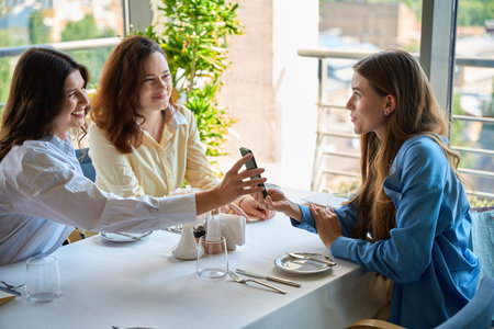 Smiling young woman talking with friends and holding smartphone in the restaurantの写真素材