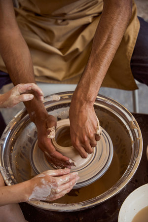 Adult male and child shaping clay on pottery wheel indoors