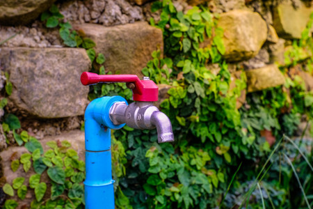 Red faucet, blue plastics pipe Stone wall backgroundの写真素材